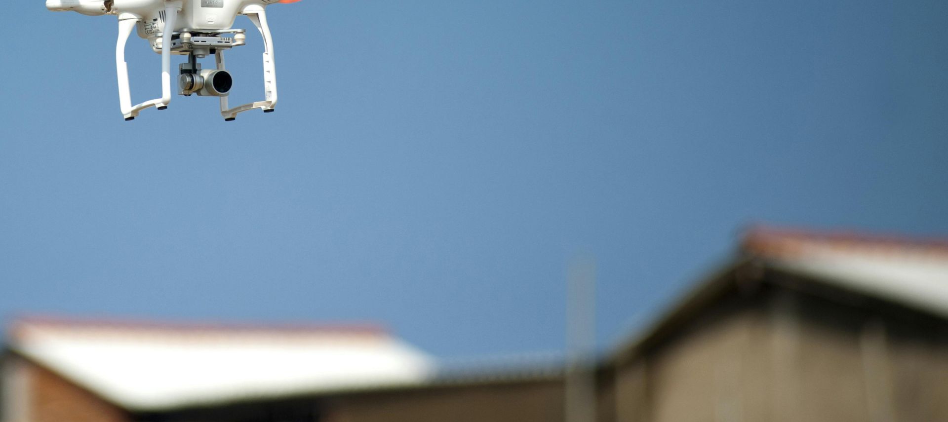 Aerial drone with camera hovering over rooftops beneath a clear blue sky, showcasing modern technology in action.